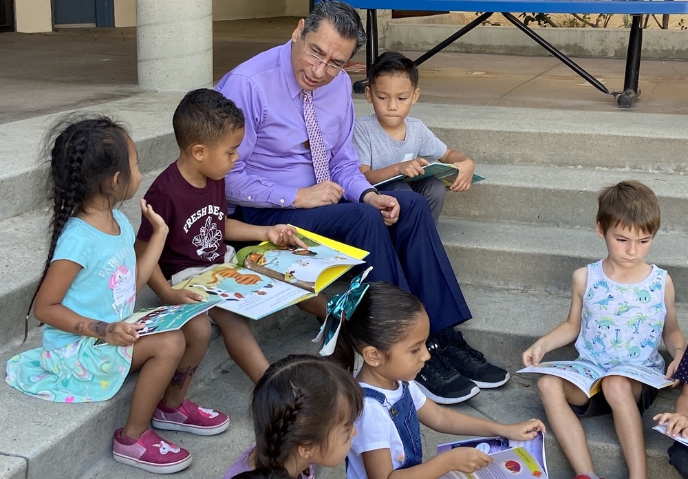 hombre sentado con niños en pasos concretos al aire libre mirando libros