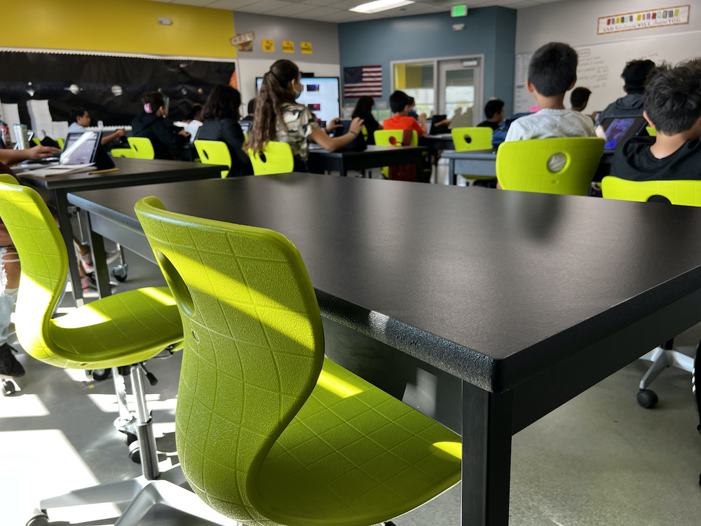 view of classroom with black tables, green chairs, backs of students