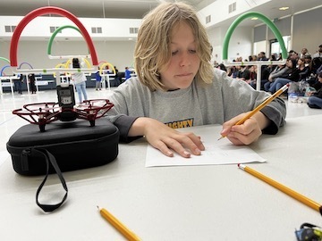 boy writing at table with drone next to him