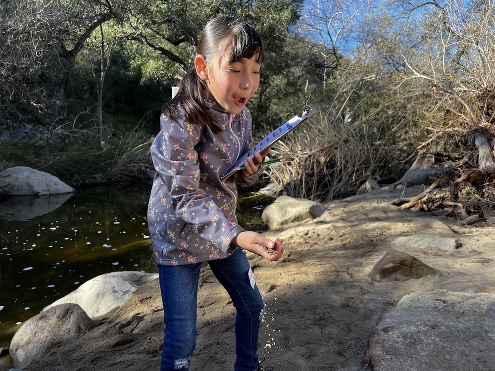 girl holding clipboard smiling next to creek