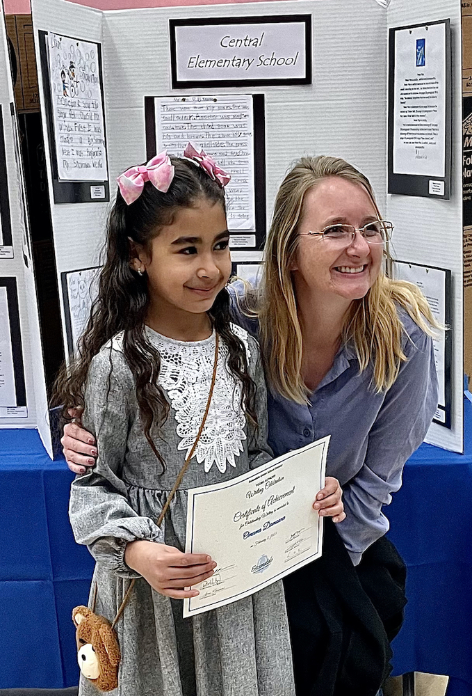 niña sosteniendo un certificado sonriendo con el maestro