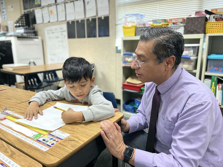 superintendent kneeling at desk looking at boy student's work