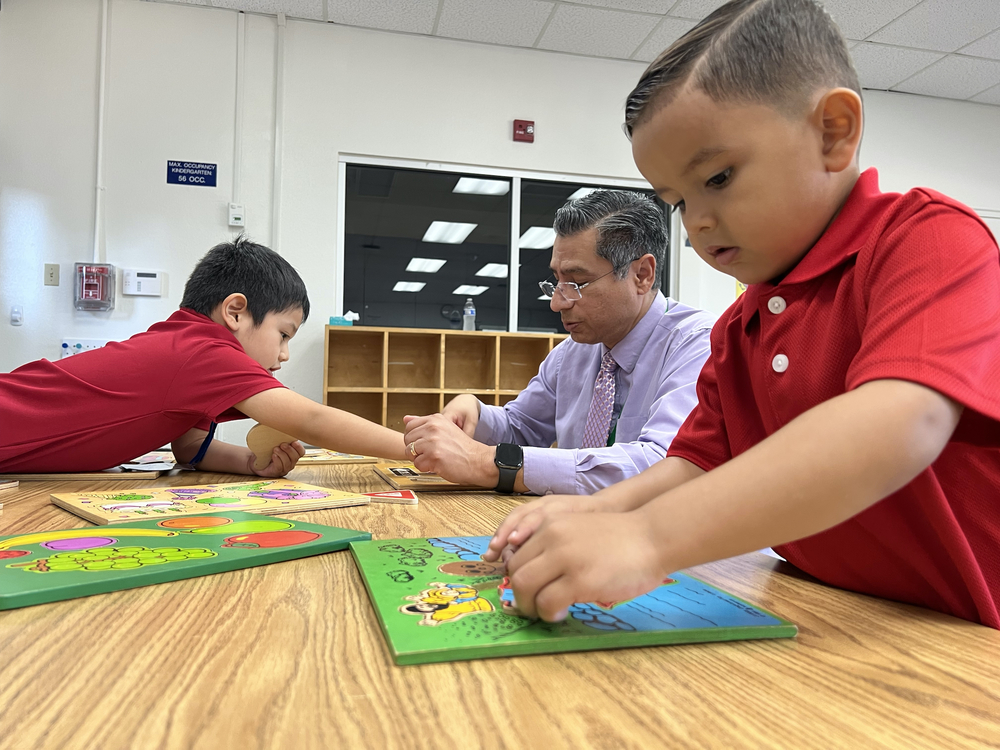 two preschool boys in red shirts doing puzzles with man in lavender shirt at classroom table