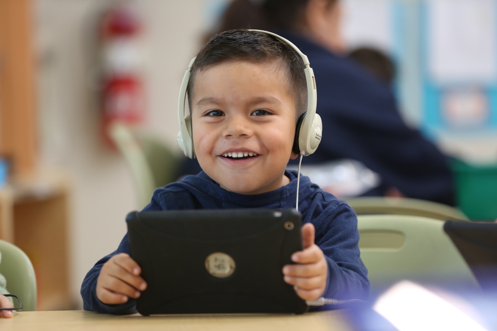 smiling young boy wearing headphones holding ipad 