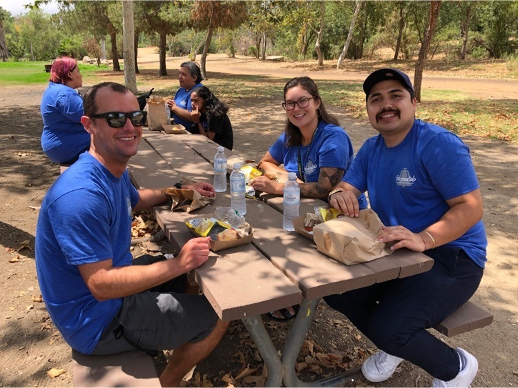 two men, one woman in blue shirts at picnic table 