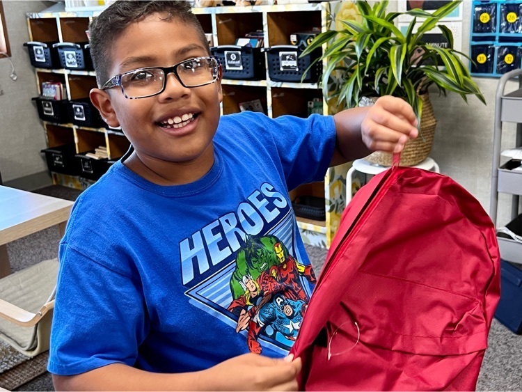 boy in blue t-shirt with glasses opening red backpack