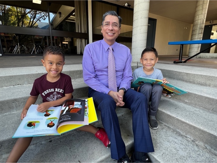 superintendent sitting between two boy students holding books