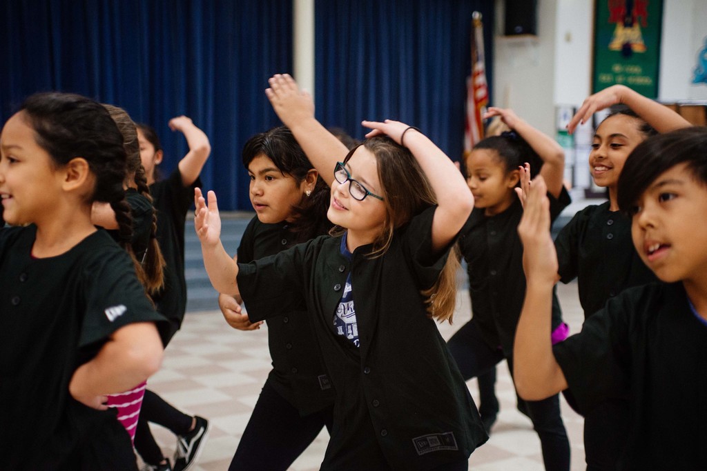 young girls, boy dressed in black in a dance pose