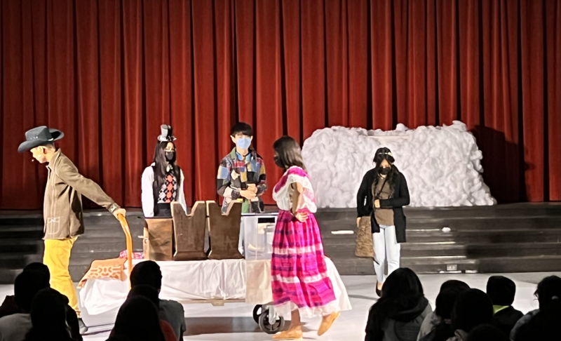 Student actors in costume during a performance in front of an audience.