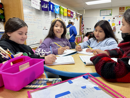 three girls smiling at table in classroom