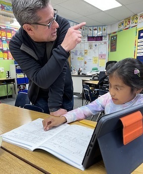 male teacher with glasses leans in to help girl with math