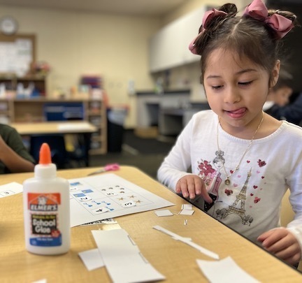preschool girl at table with glue bottle and paper