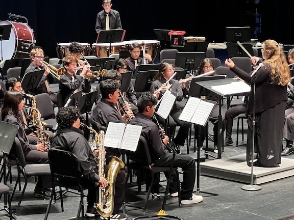 wide view of middle school musicians on stage with teacher conducting
