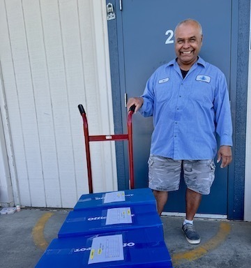 man in blue uniform shirt standing smiling with cart carrying boxes