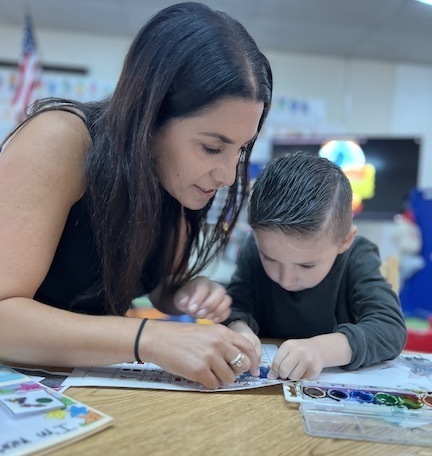 teacher leaning in with boy student painting